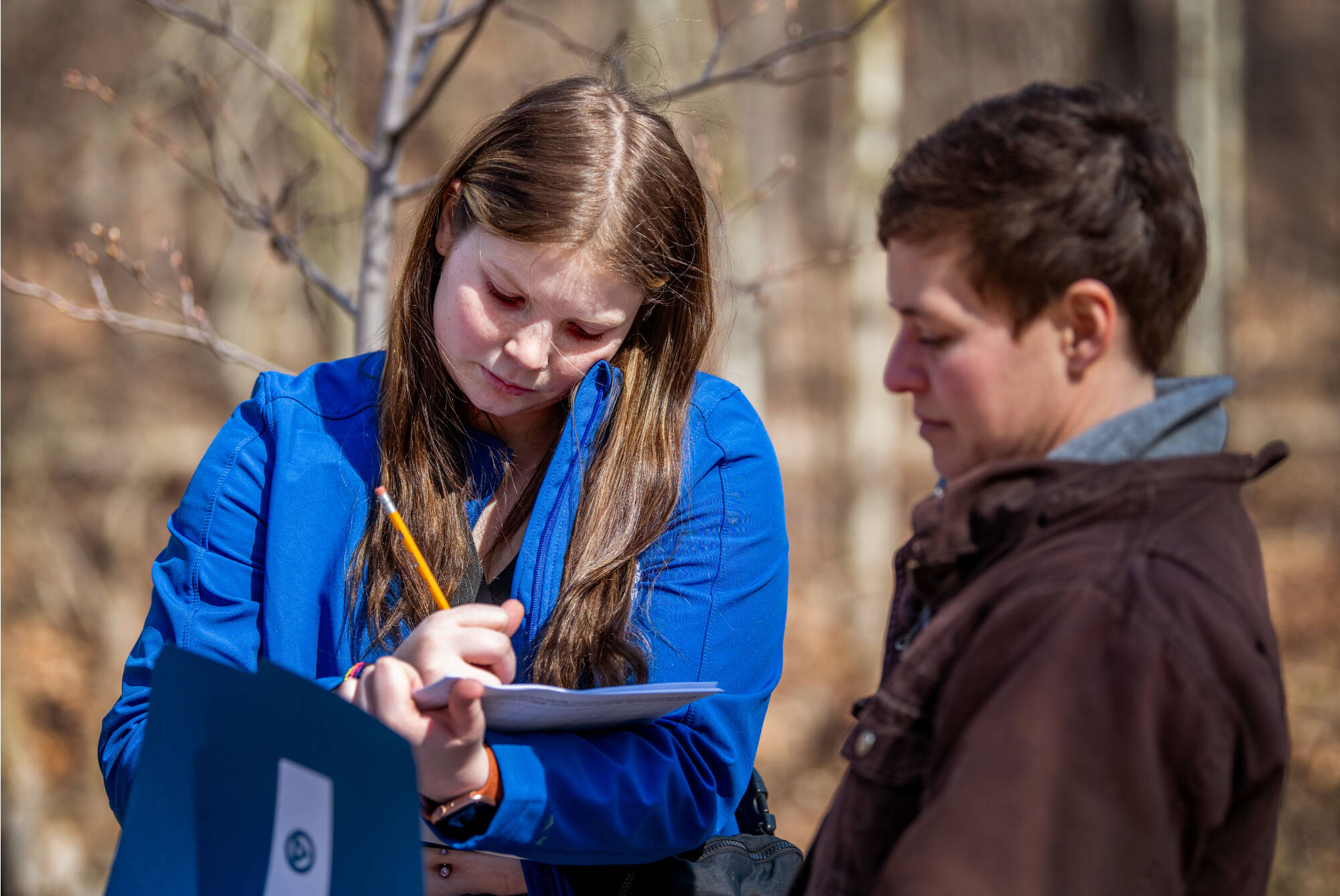 Student fills out a clipboard with a scientist standing next to the student providing guidance